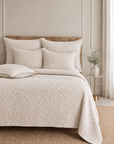 Oatmeal beige matelasse quilt with matching shams and pillows on a bed.