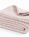 Matelasse quilted throw blanket in blush pink, neatly folded with texture