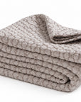 Folded oatmeal-beige matelasse quilt with textured raised pattern.