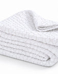Folded white matelasse blanket/quilt with layered edges and textured surface.