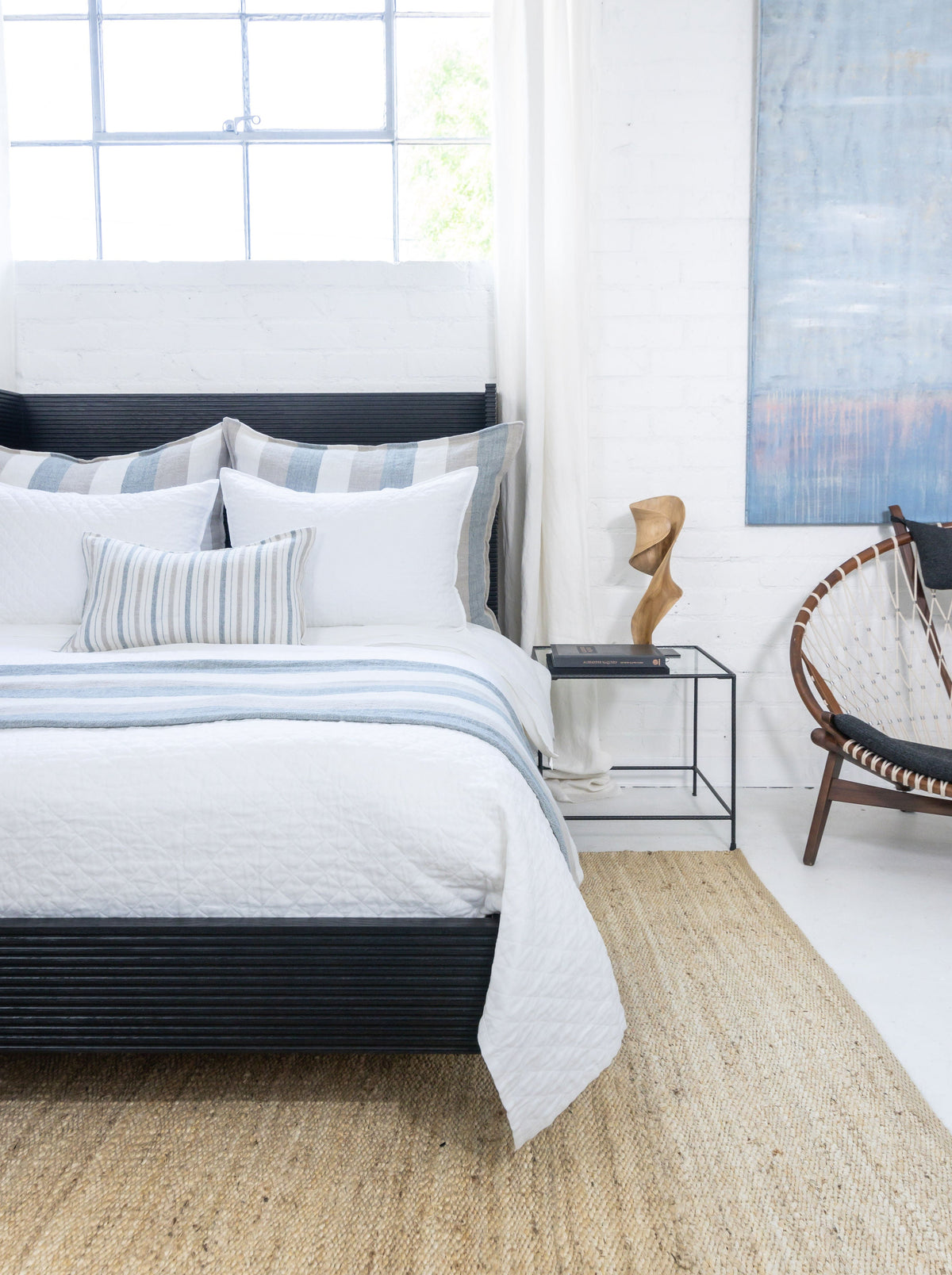 Large striped decorative pillows on bed with light blue and beige vertical stripes