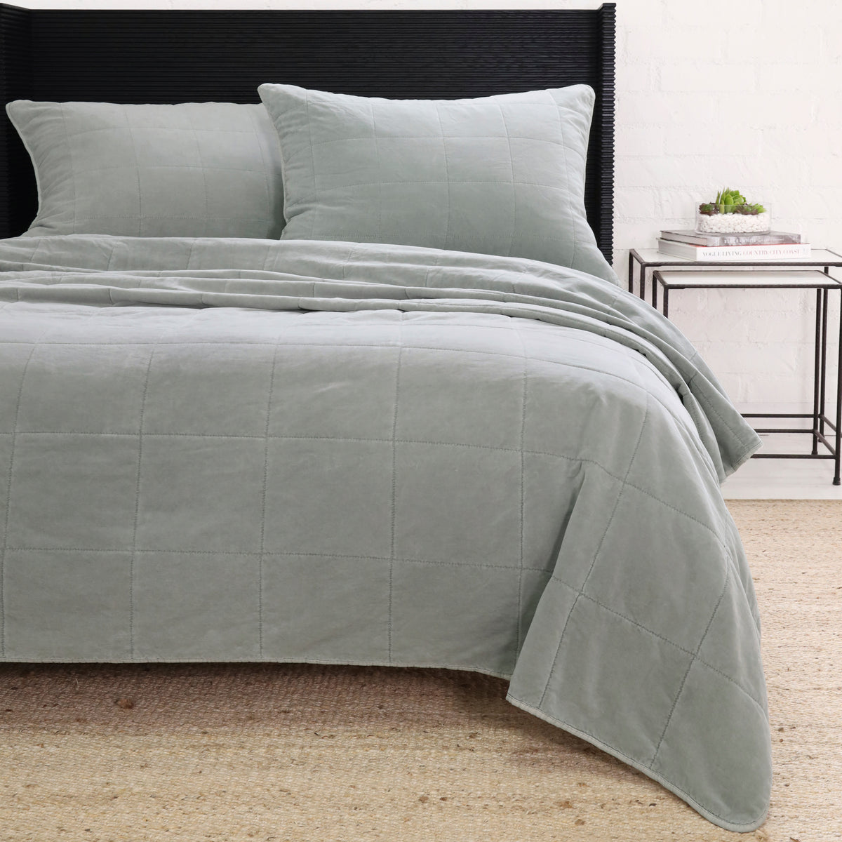 Light blue quilted coverlet draped over bed with matching pillow shams
