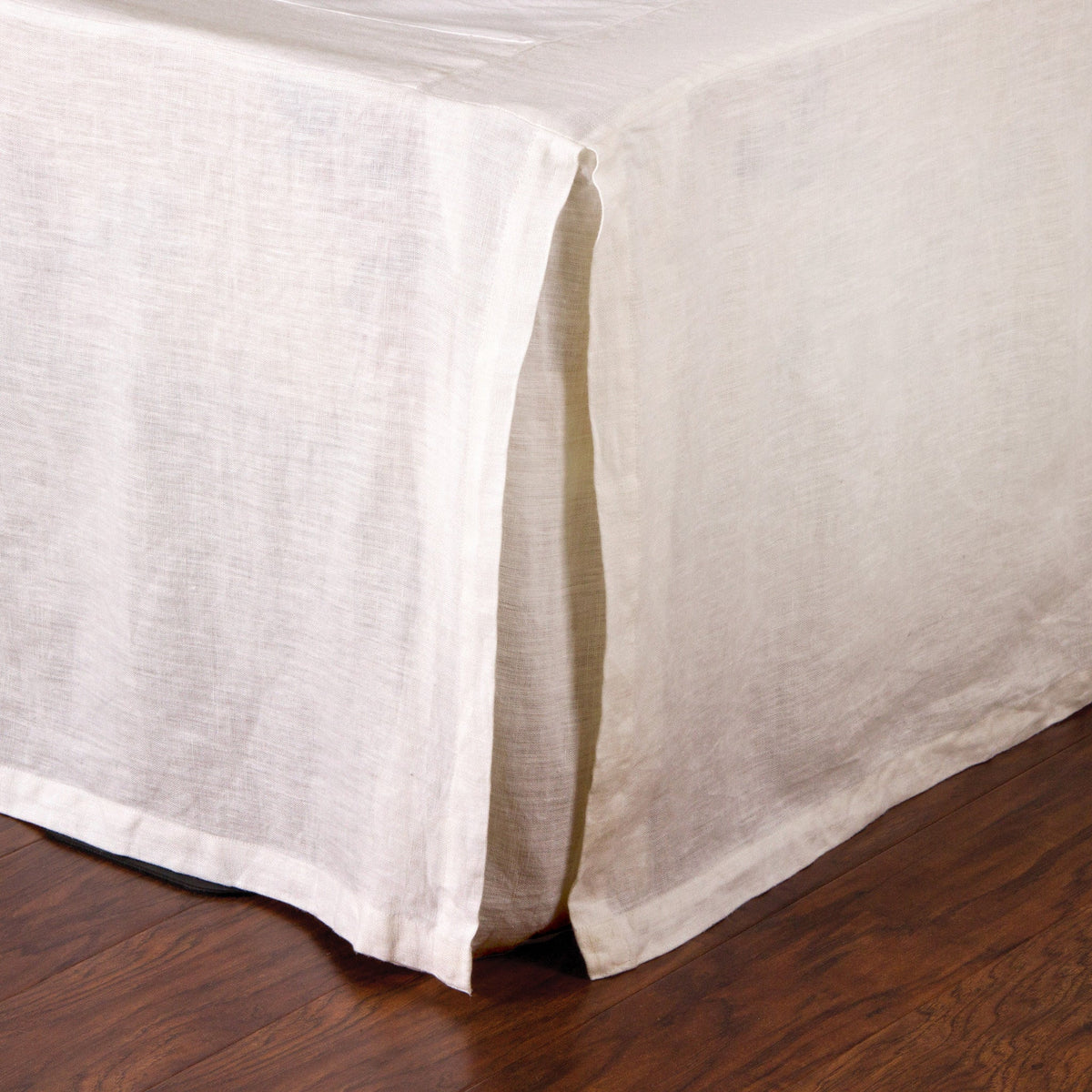 Linen bedskirt corner with clean stitched hem and vertical pleat detail near floor