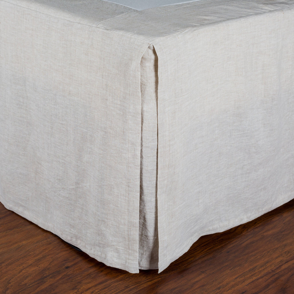 Pleated linen bedskirt corner with vertical seam/pleat and crisp straight edge hem