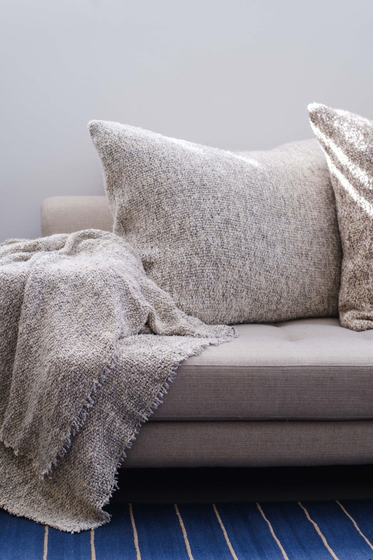 Textured throw blanket in gray with fringed edges, folded over couch arm.