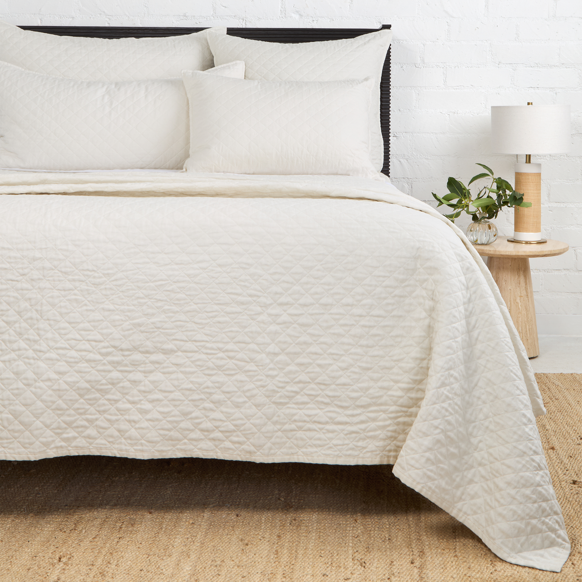 Quilted white coverlet with diamond stitch pattern, draped over bed edge
