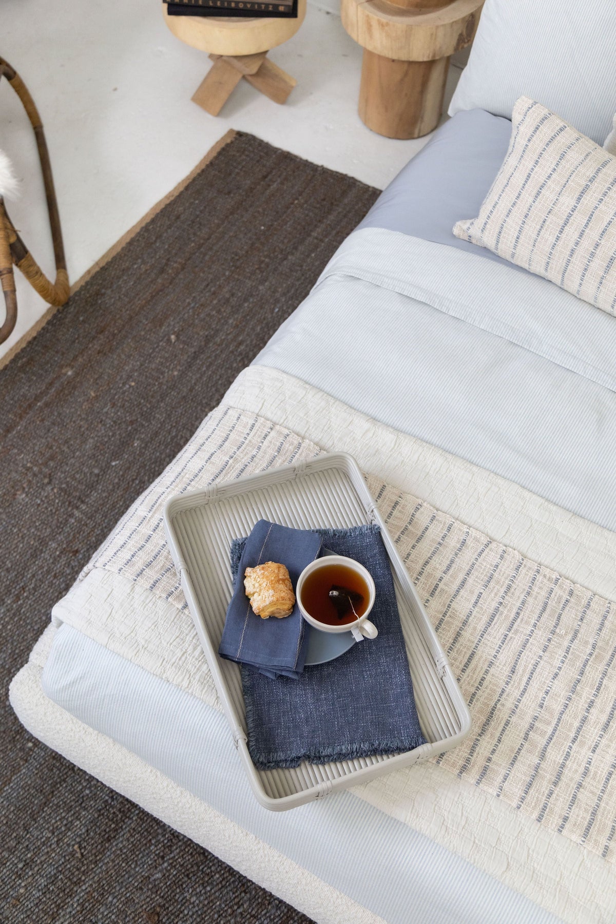 Striped woven throw blanket with fringe draped on a bed in light blue and ivory