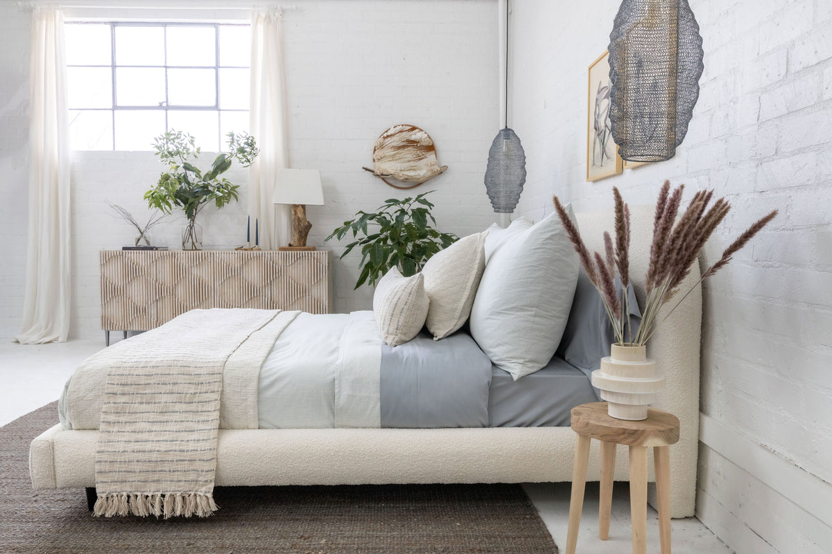 Ivory and light blue striped throw with fringe draped over a bed