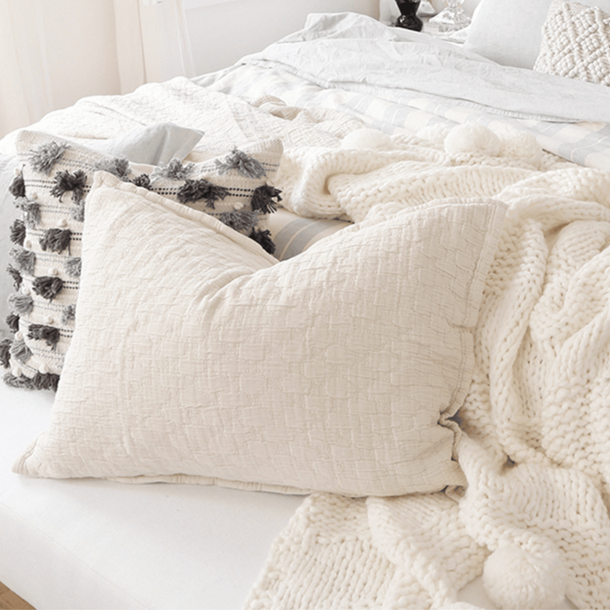 Cream matelasse quilt with textured pillows and soft pom-pom accents