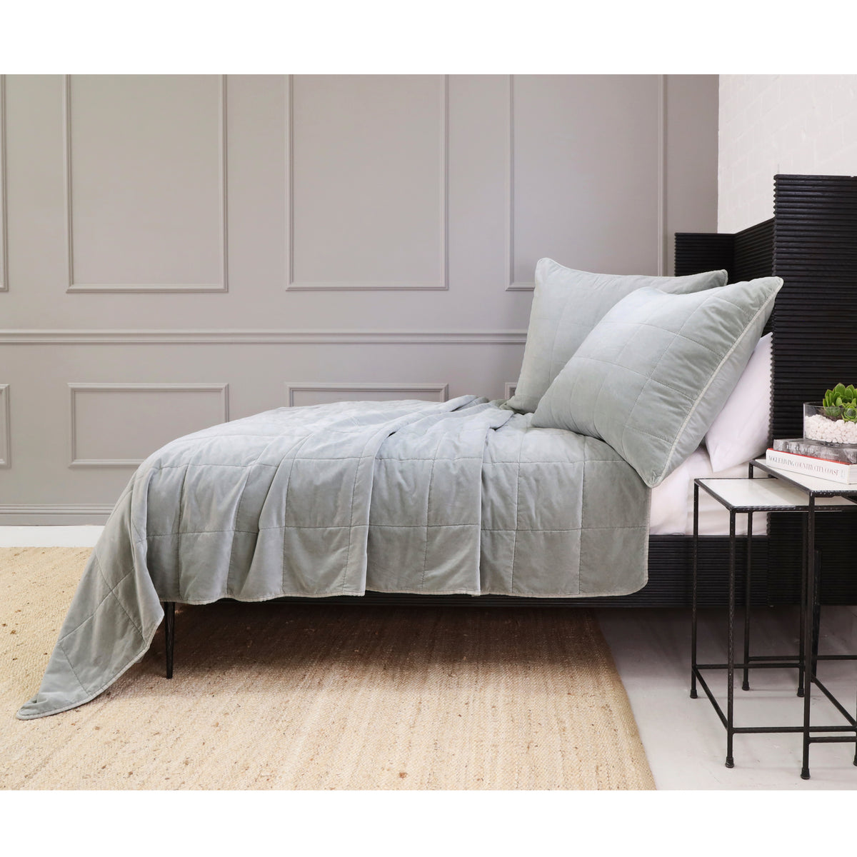 Light gray quilted coverlet and pillows on bed with layered throw drape