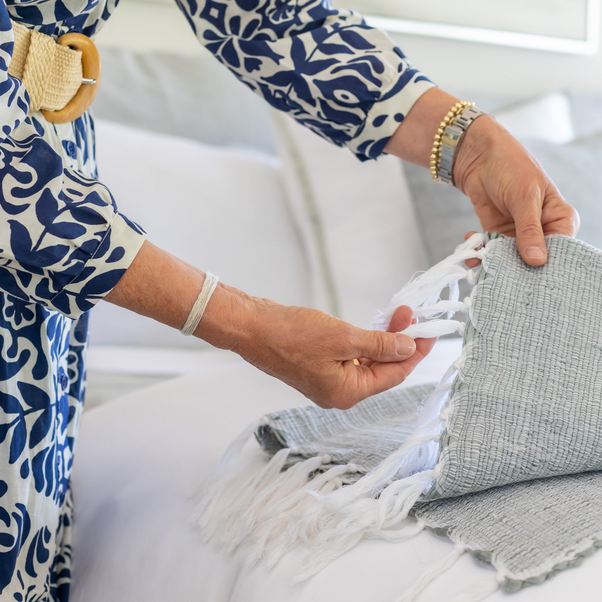 Hands adjusting Shore Blue woven throw corner with white tassel fringe