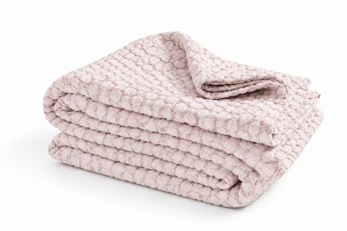 Matelasse quilted throw blanket in blush pink, neatly folded with texture