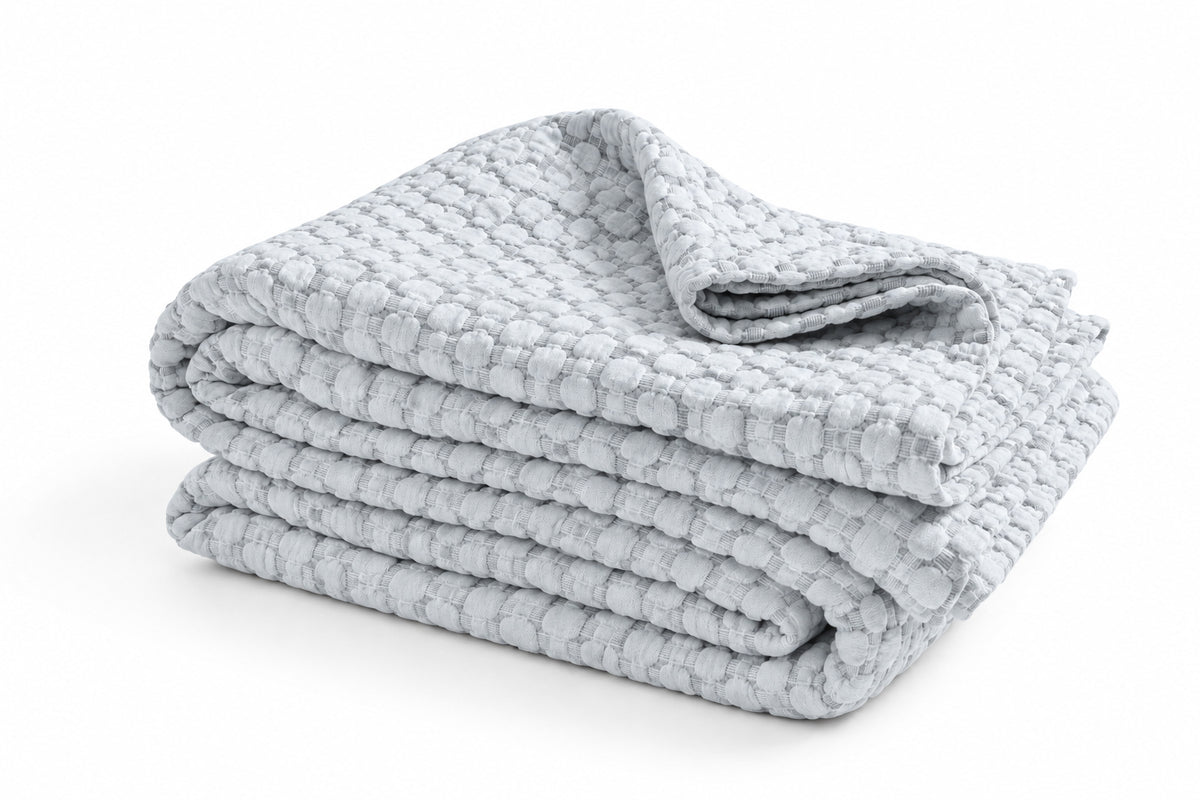 Matelasse quilted throw blanket in light blue, folded stack with texture