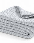 Matelasse quilted throw blanket in light blue, folded stack with texture