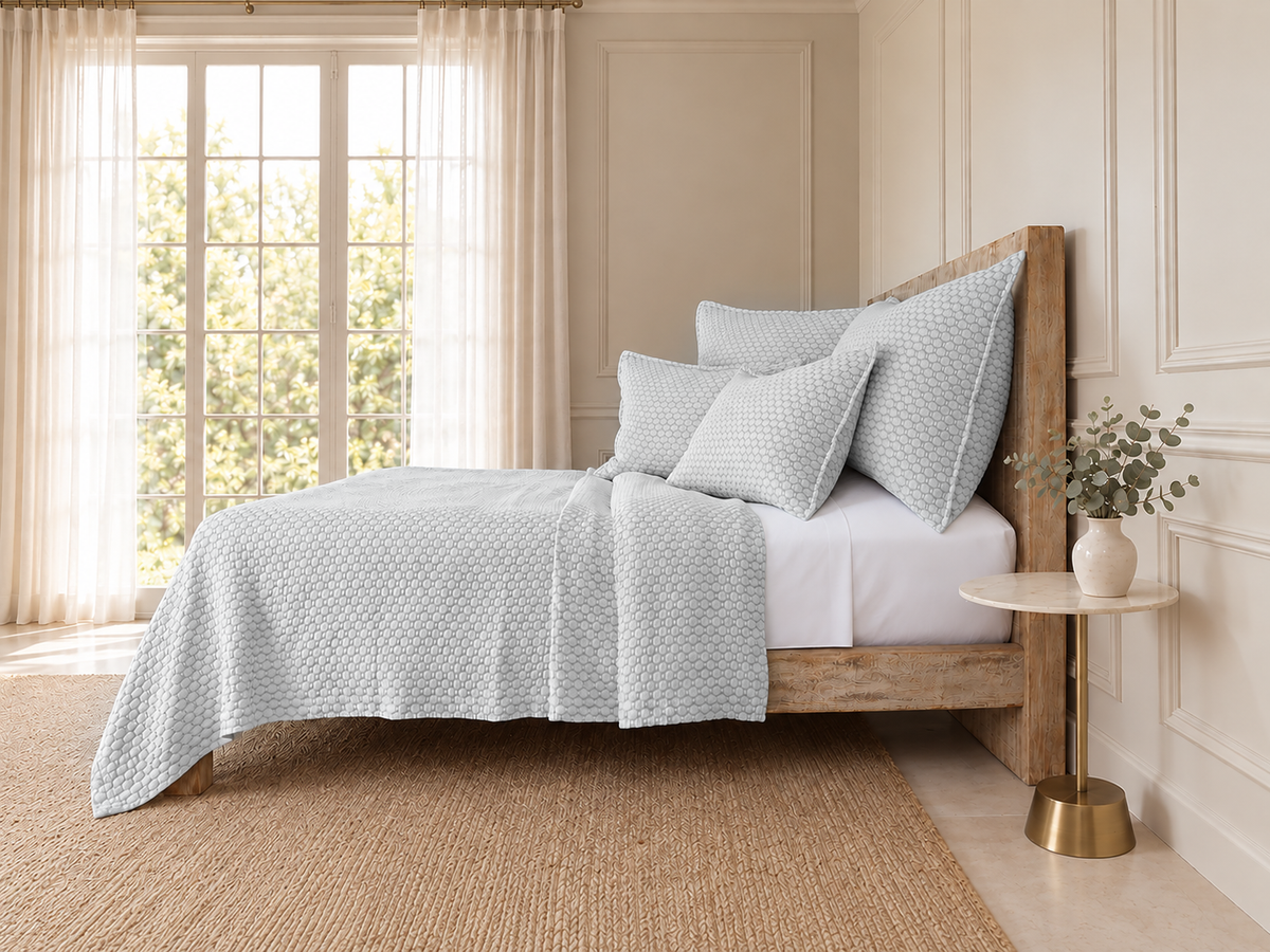 Light blue matelasse quilt with matching textured shams and pillows on a bed.