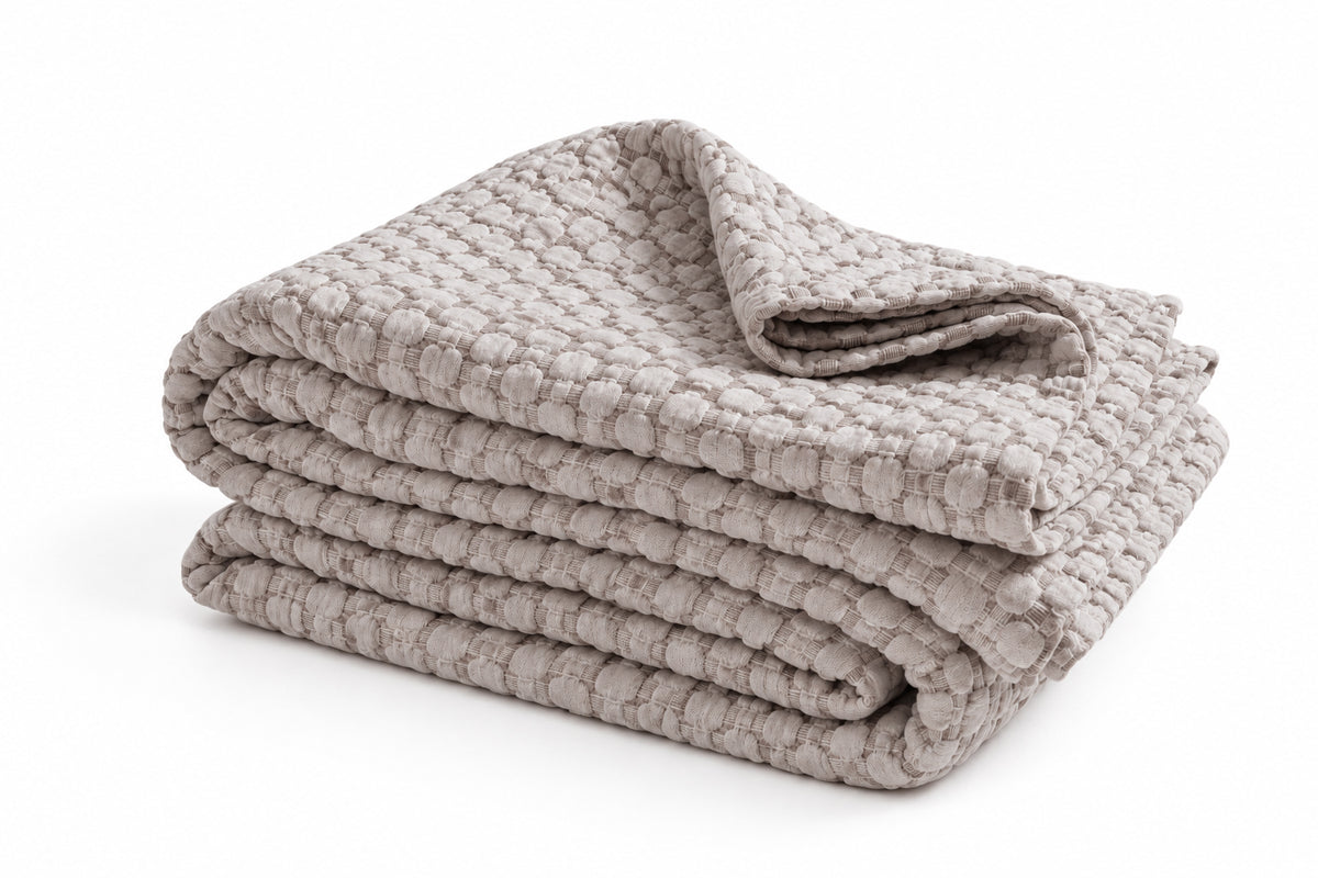 Folded oatmeal-beige matelasse quilt with textured raised pattern.