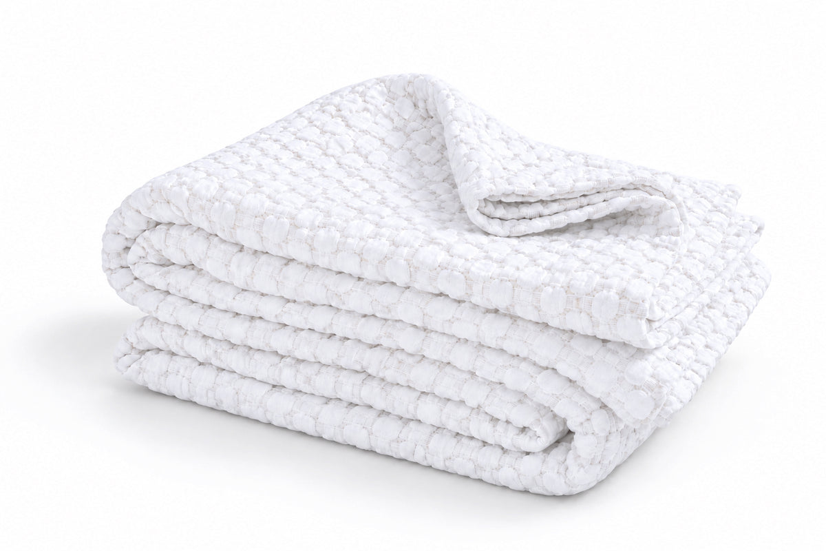 Folded white matelasse blanket/quilt with layered edges and textured surface.
