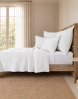 White matelasse bed quilt with textured geometric pattern and matching pillow shams