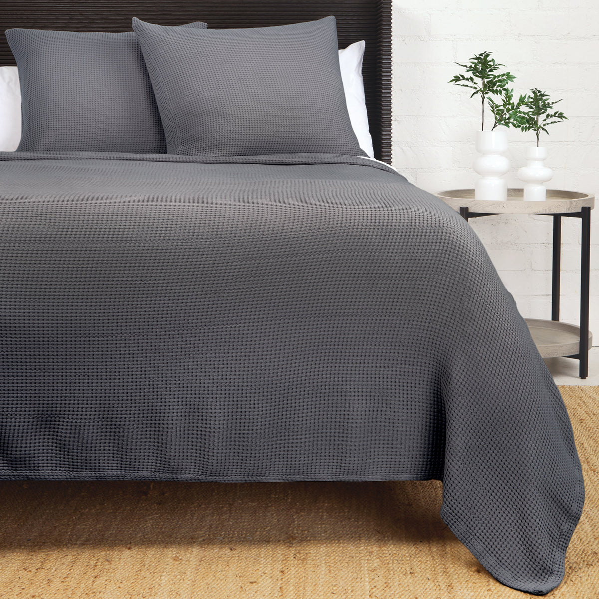 Textured woven blanket in dark gray, draped over bed with two matching pillows.