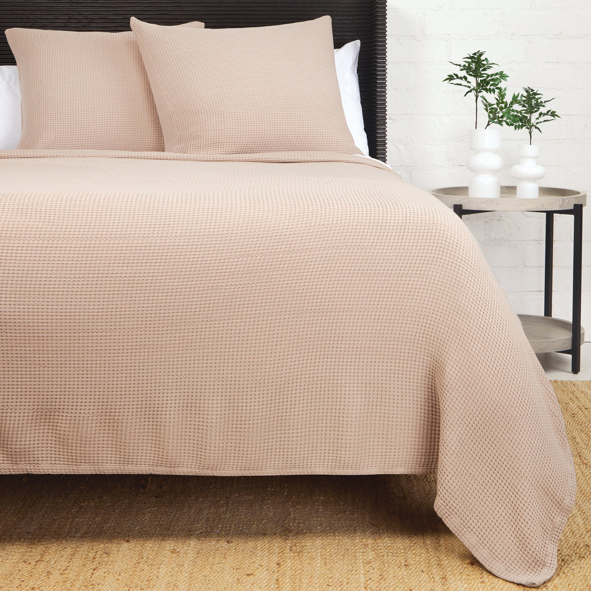 Textured woven blanket in sand, draped over bed with two matching pillows.