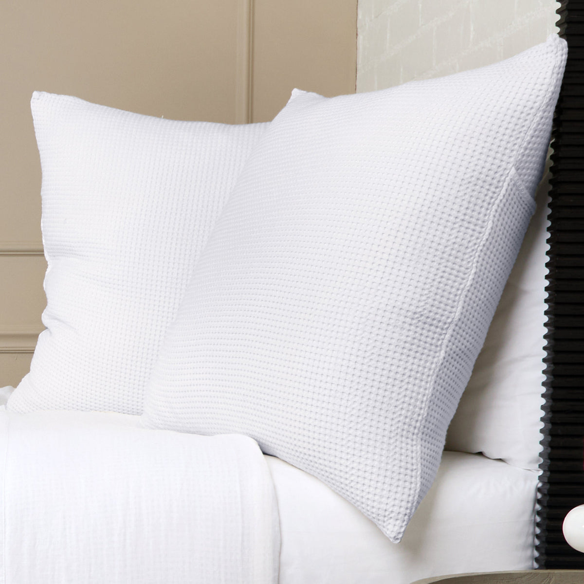 White textured pillow on bed, featuring a woven waffle-like fabric texture.