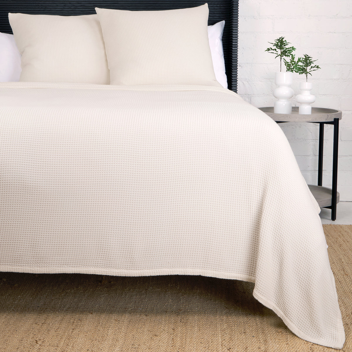Textured woven blanket in white, draped over bed with two matching pillows.