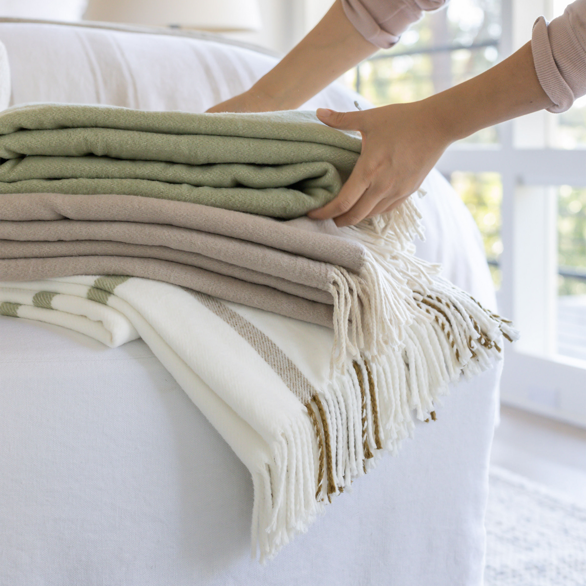 Plaid throw blankets in green and white with fringed edges, stacked on sofa