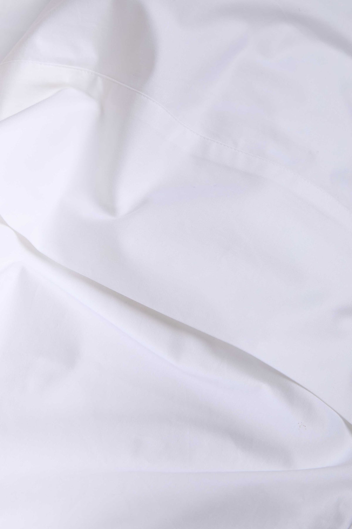 White cotton sateen sheet fabric close-up with stitched seam and soft drape