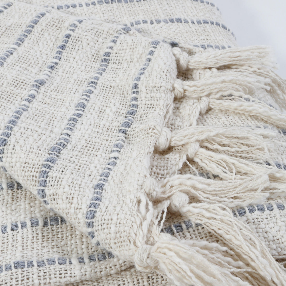Ivory and blue-gray woven throw close-up with textured stripes and tassel fringe