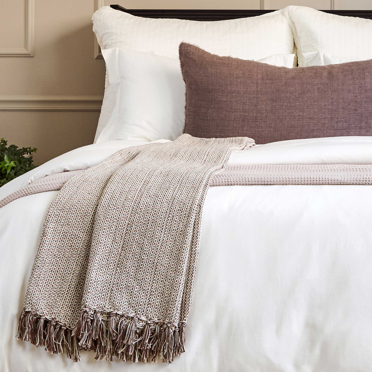 Blue-grey woven throw blanket with fringe edge draped over bedding