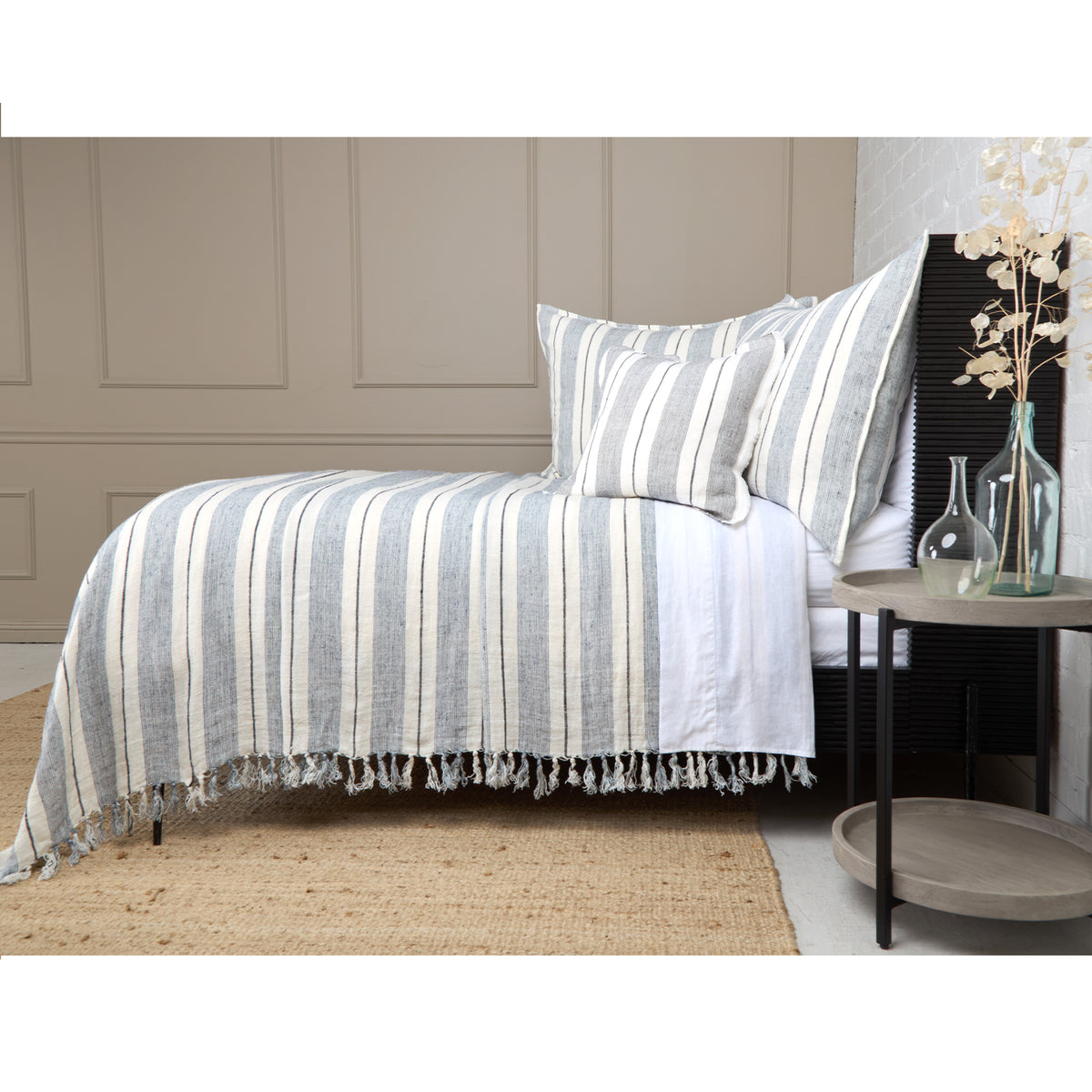 Striped blanket with fringe trim in grey and natural on a bed