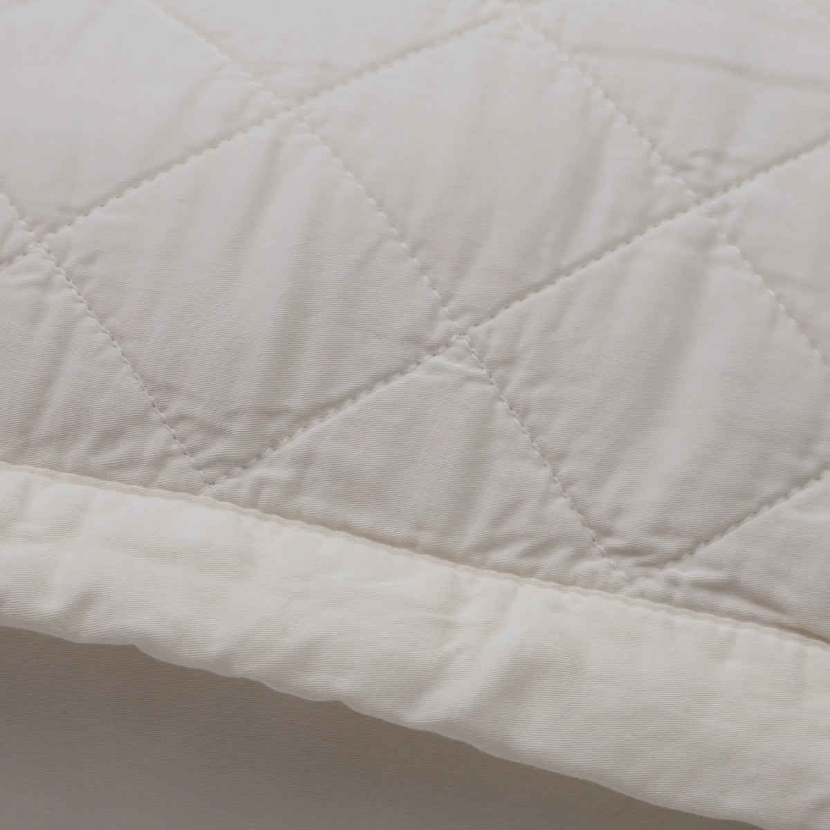 Close-up of quilted diamond stitching on an ivory-cream pillow cover.