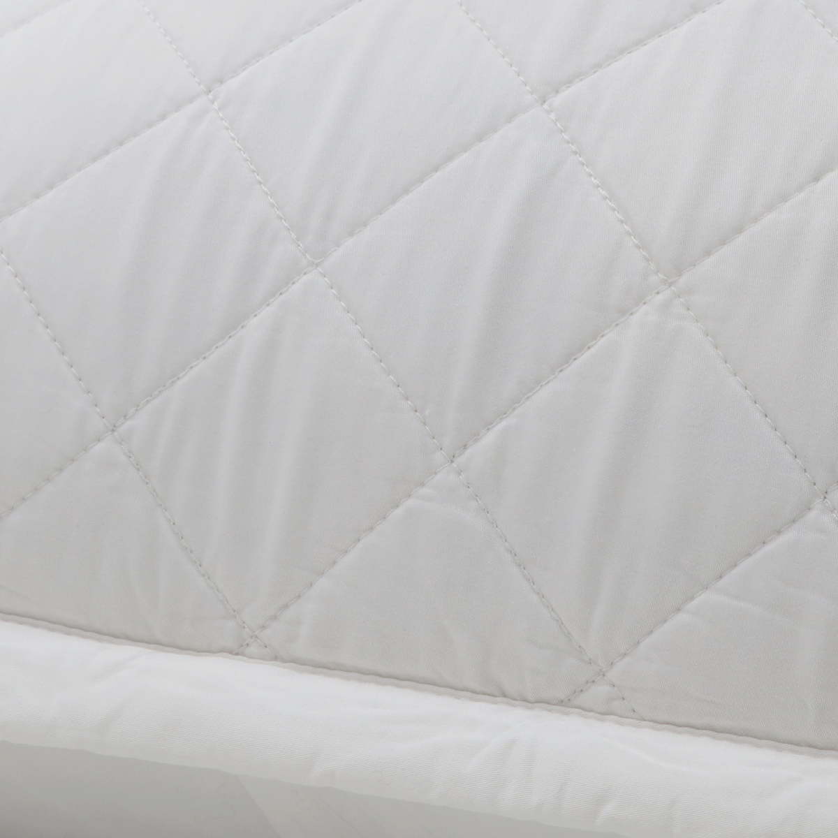 Close-up of quilted diamond stitching on a light-colored pillow cover.
