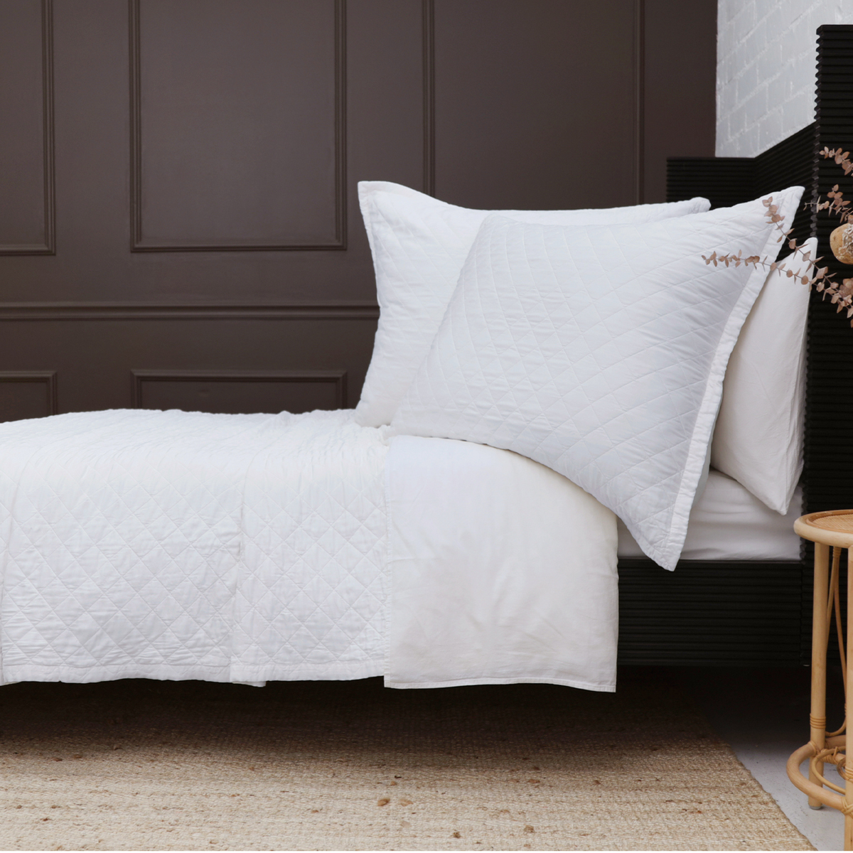 Rectangular white big pillow with stitched diamond pattern on a bed.