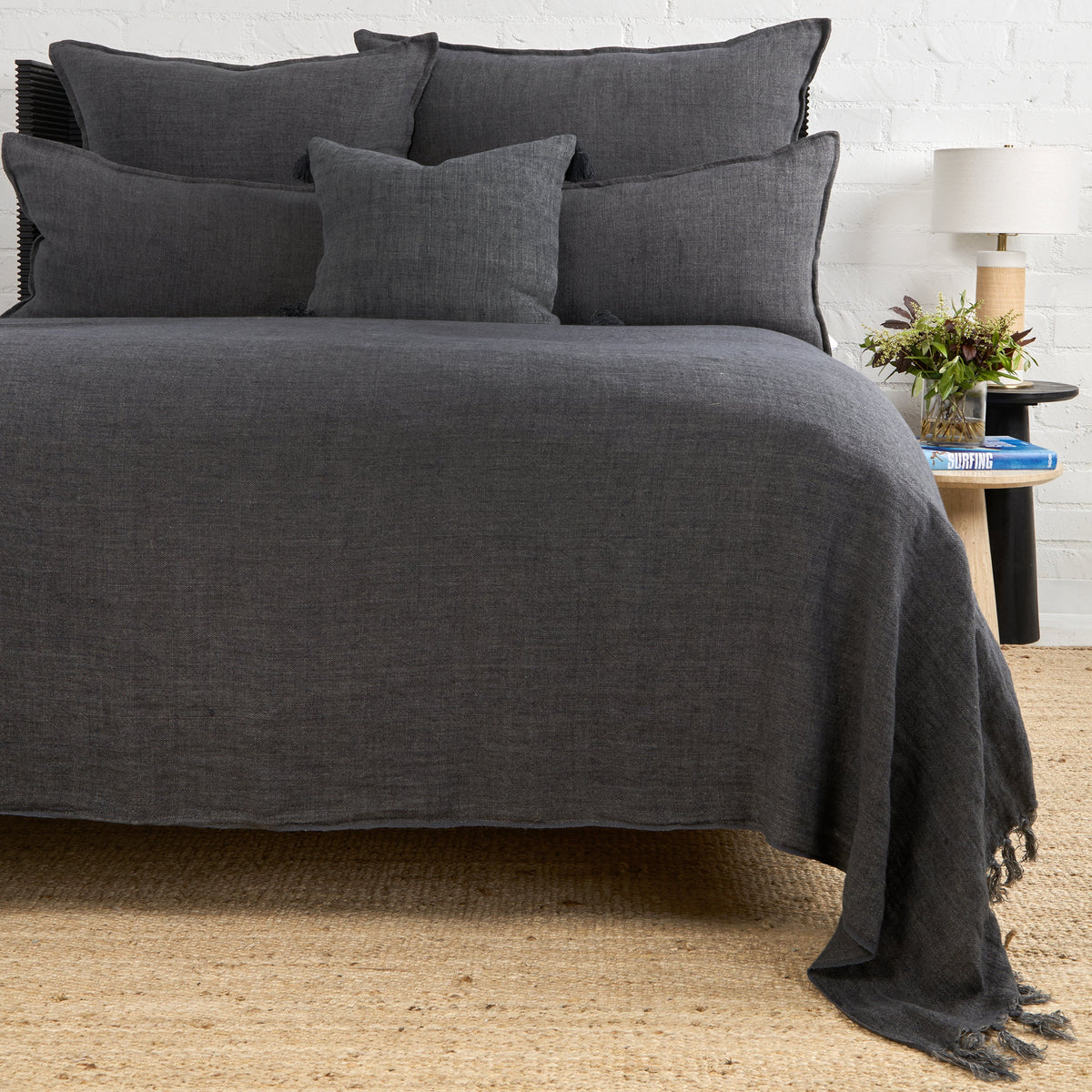Charcoal textured blanket with fringed edge draped over bed