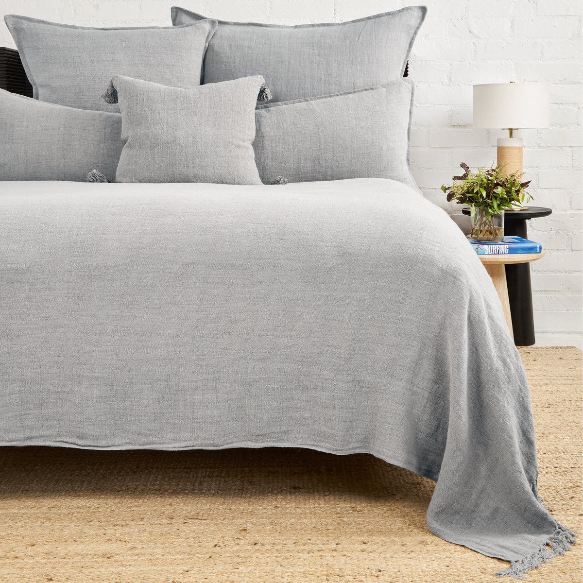 Light gray textured blanket with fringed edge draped over bed