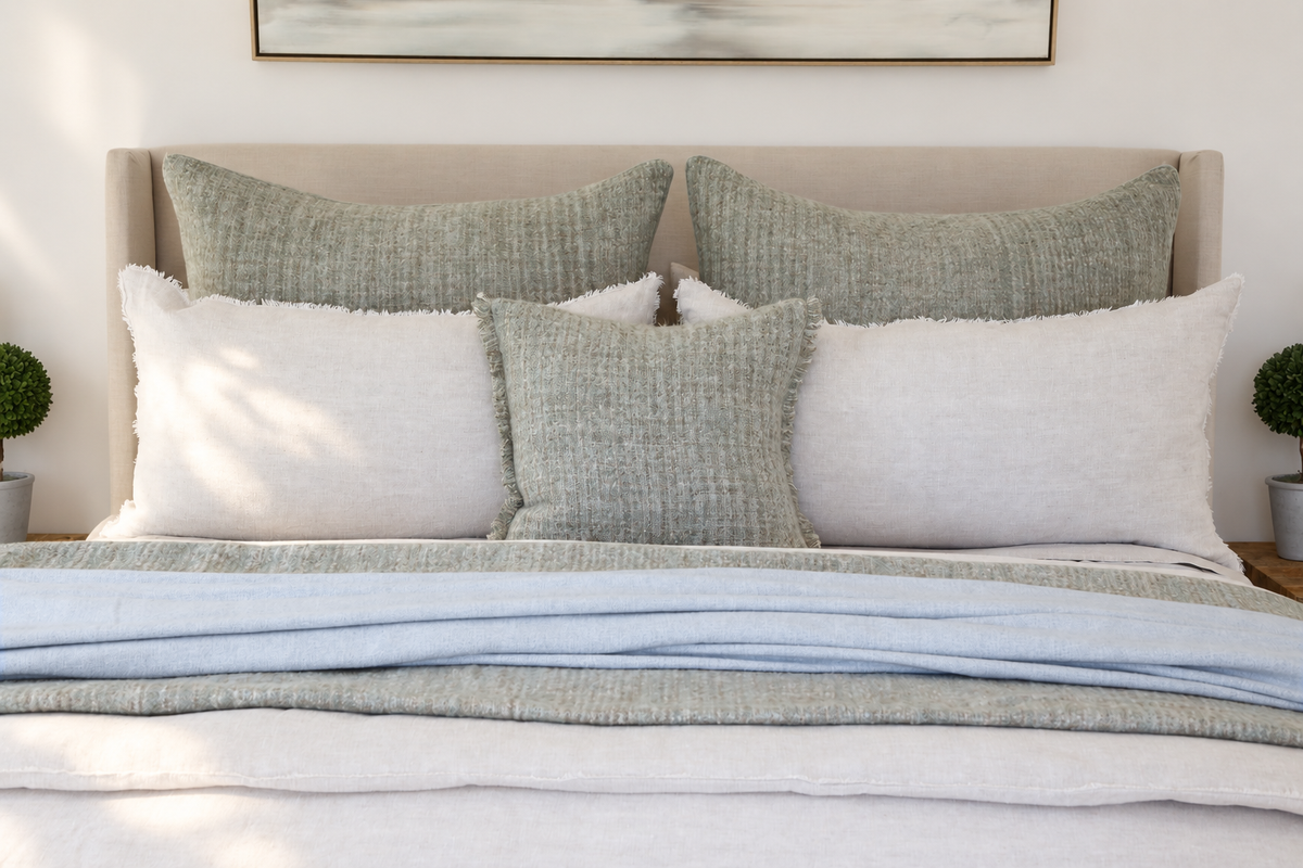 Two rectangular decorative pillows with light gray-green textured covers on bed
