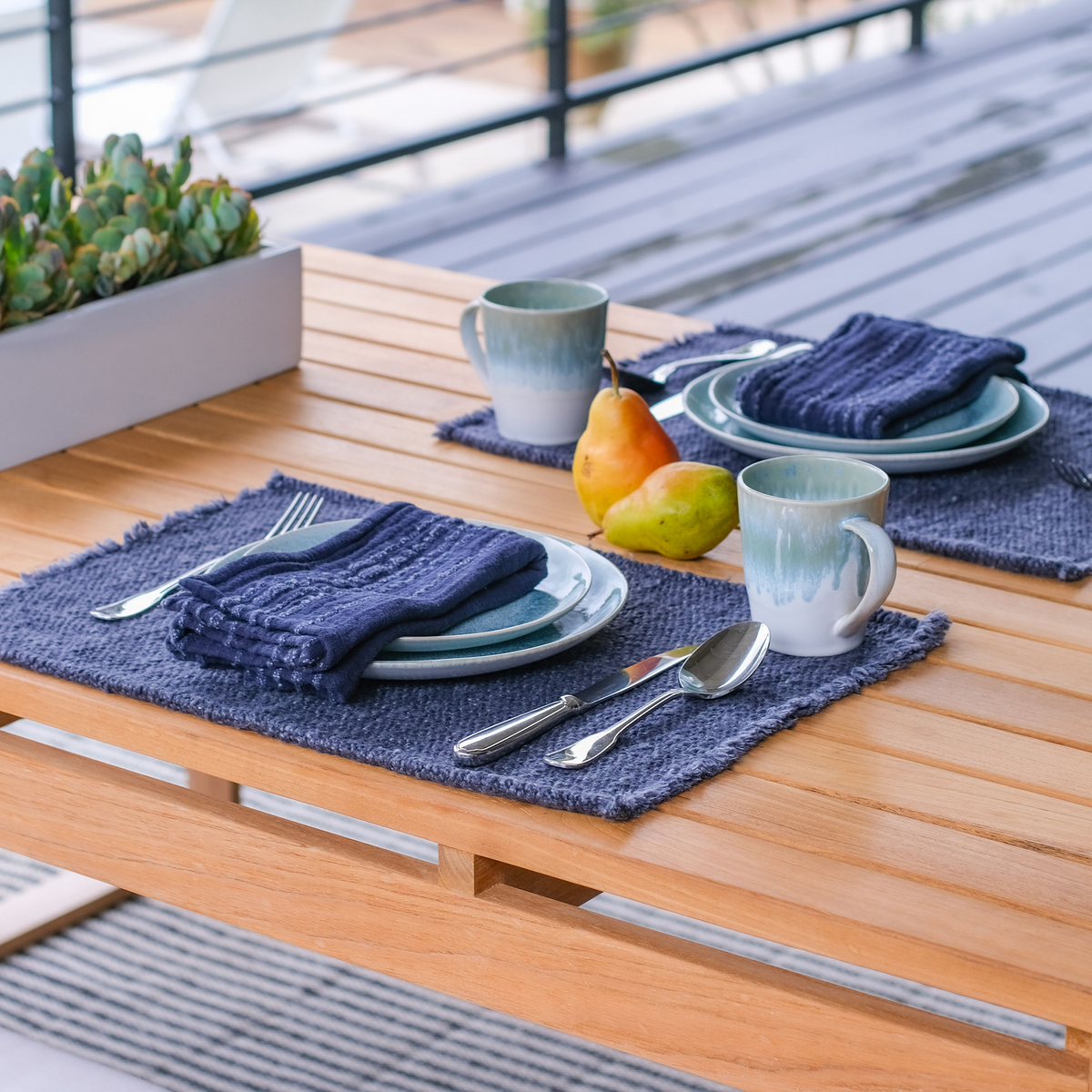 Navy placemats on wooden table with dishes and drinks; fringed woven texture