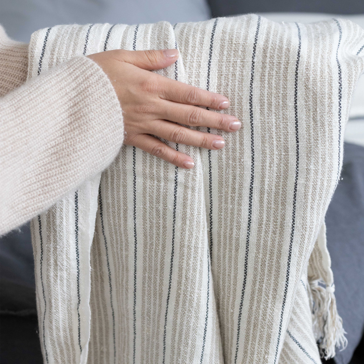 Beige and navy-striped throw blanket held by hand, showing woven texture and fringe
