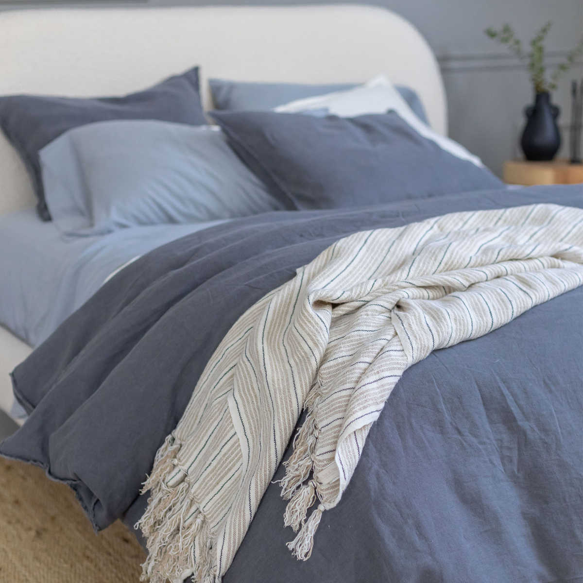 Striped woven blanket with tassel fringe, draped over bed with vertical gray lines
