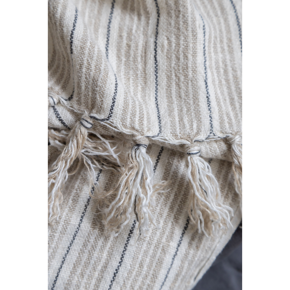 Close-up of striped blanket corner with knotted fringe and vertical gray lines
