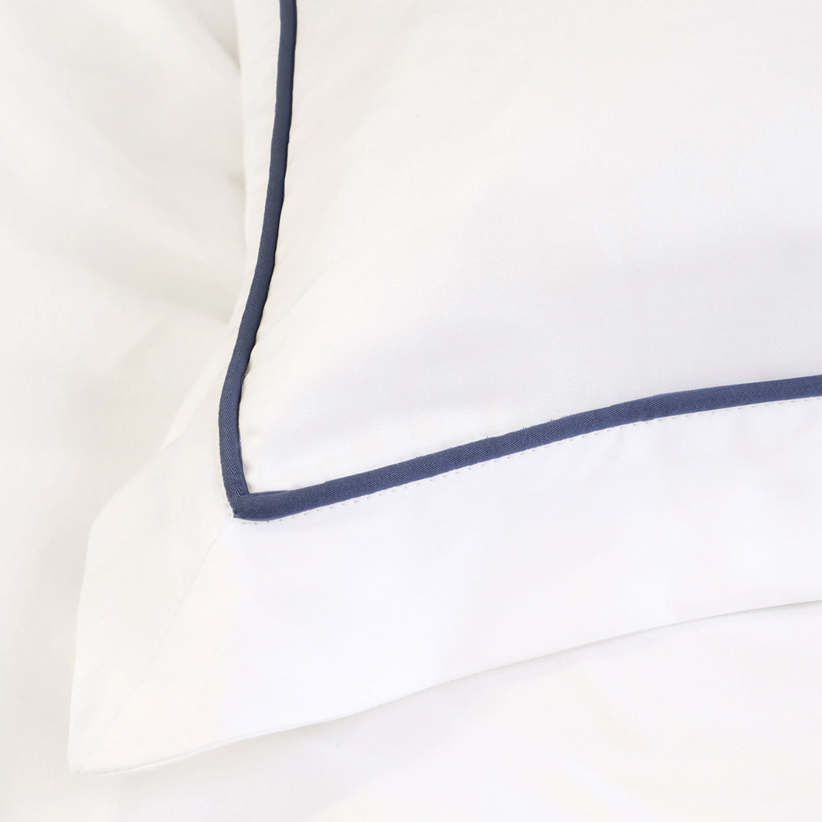 White sheet corner with navy contrast piping, smooth sateen weave