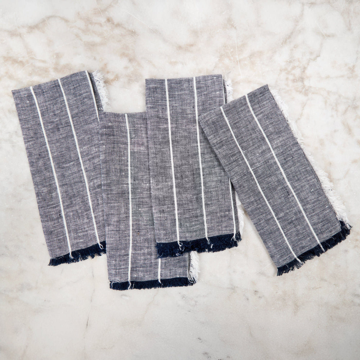 Light grey linen napkins set with thin white stripe bands and frayed edges