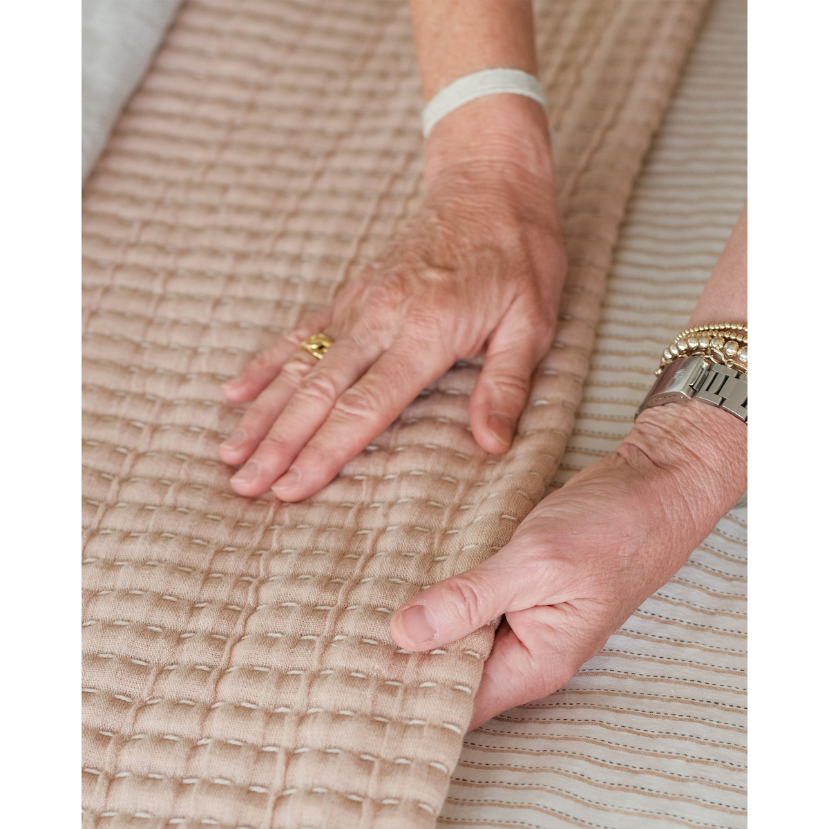 Beige textured coverlet fabric close-up with hands smoothing weave