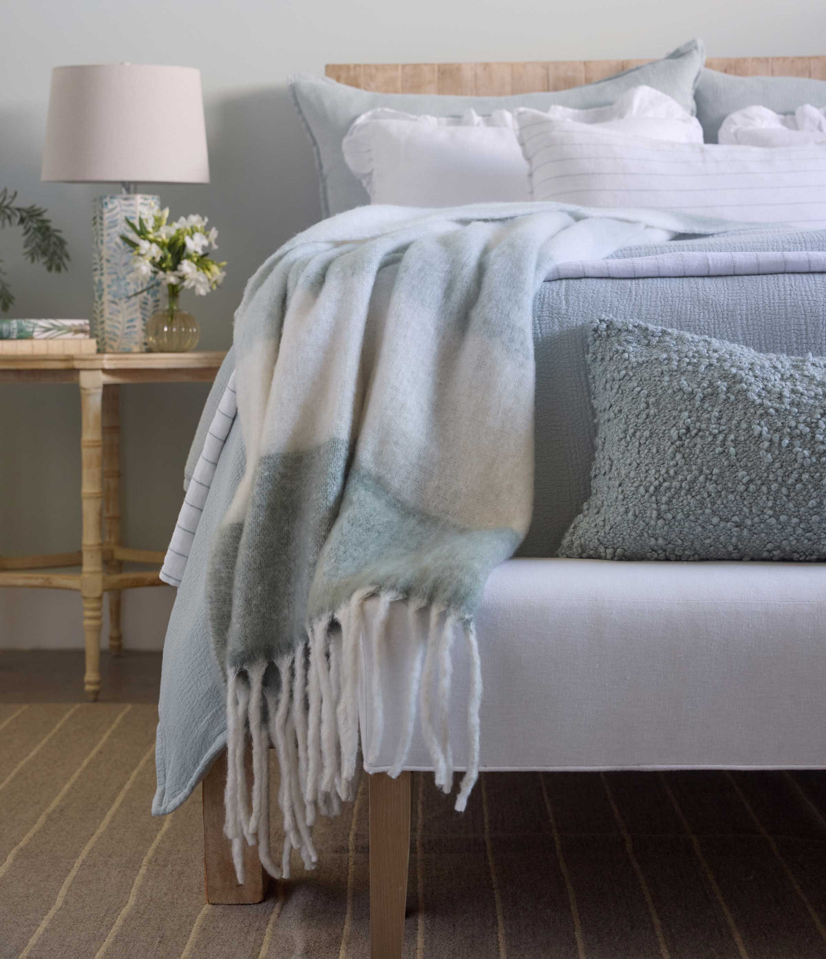 Draped throw blanket in moss tones with fringed edge, layered over a sofa backrest
