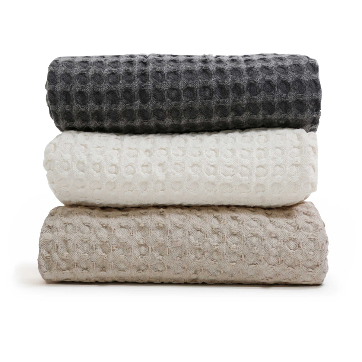 Stack of waffle-knit throw blankets in charcoal, cream, and natural shades